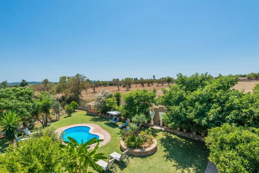 A garden surrounds a curved swimming pool and landscaped greenery.