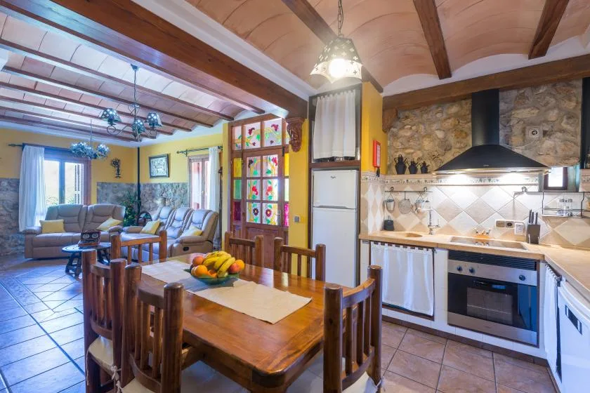An open-plan kitchen and dining area with a wooden dining table and stone backsplash.
