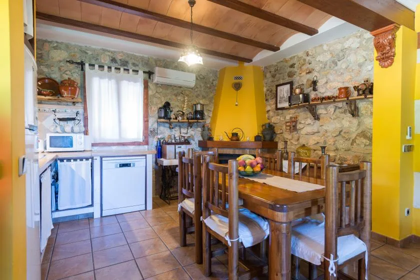 A rustic kitchen and dining area with a wooden table and exposed stone walls.