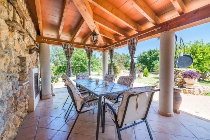 A covered outdoor dining area has a long table beneath a timber roof.