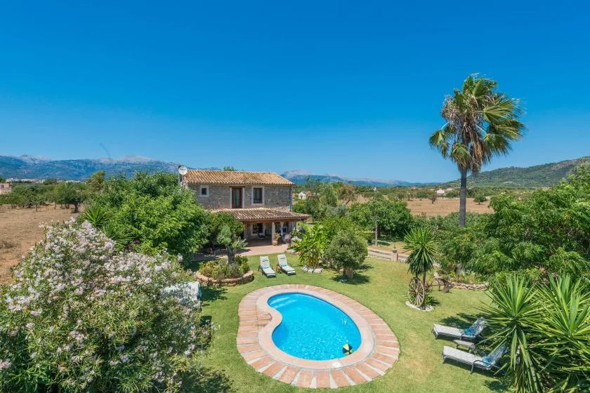 A garden surrounds a small swimming pool beside a two-story house.