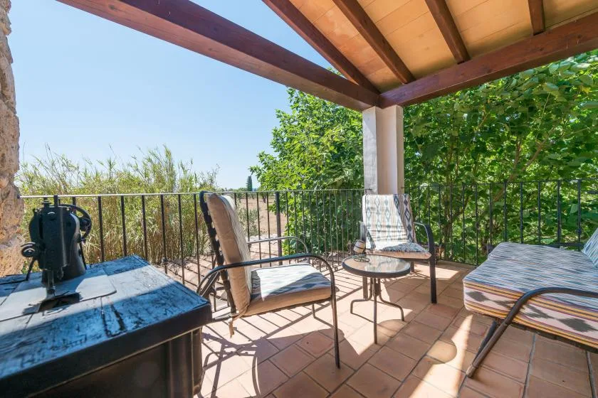 A covered patio with seating and a small table overlooks leafy greenery.