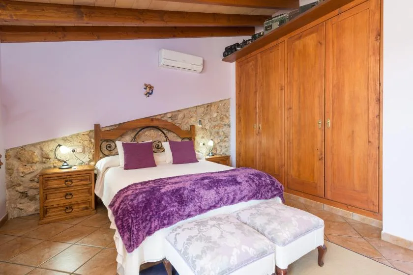 A bedroom with a double bed, purple blanket, and wooden wardrobe.