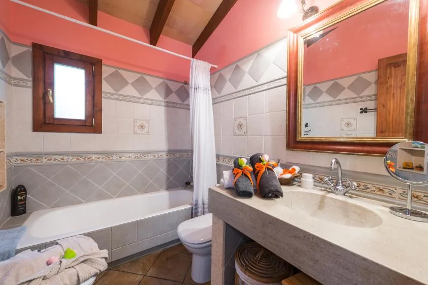 A tiled bathroom with a bathtub, toilet, and sink beneath a large mirror.