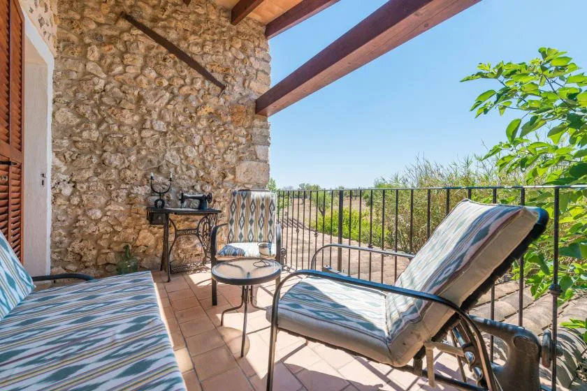 A stone-walled patio with cushioned seating and a metal railing overlooking greenery.