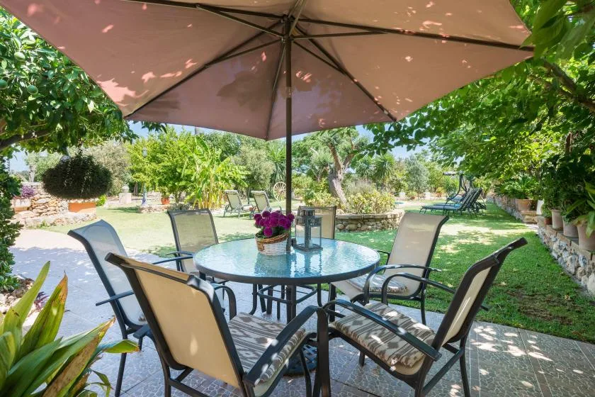 A garden patio with a round table and chairs beneath a large umbrella.
