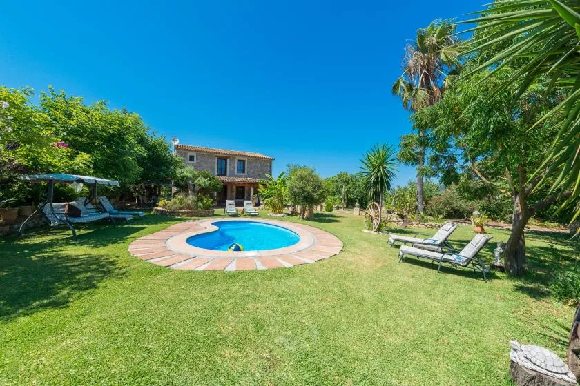 A garden surrounds a small swimming pool, with lounge seating and a house beyond.