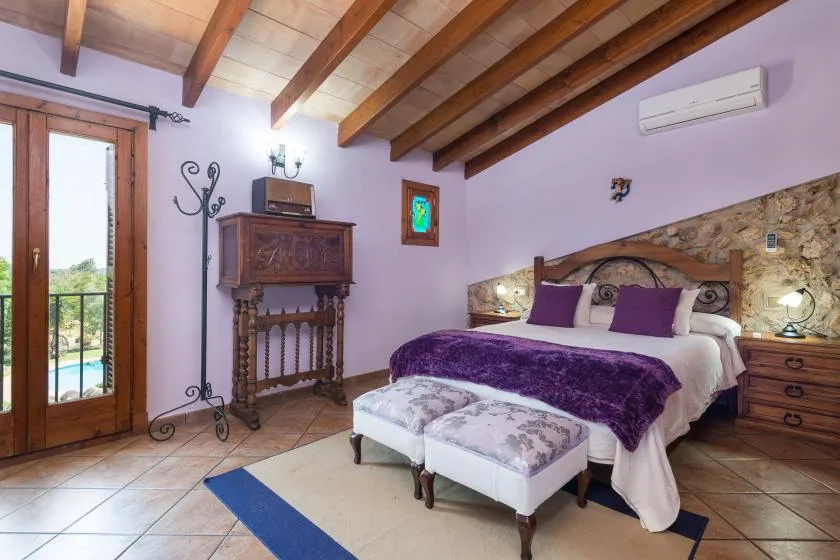 A bedroom with a double bed, purple bedding, and exposed wooden ceiling beams.