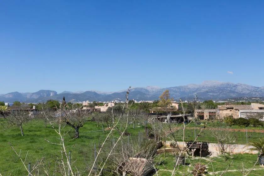 A rural landscape with green fields, scattered buildings, and mountains in the distance.