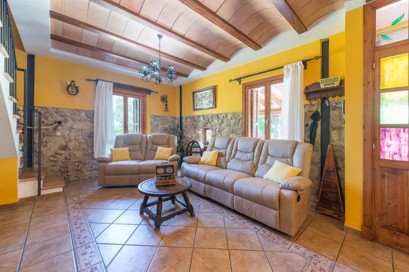 A living room with cushioned seating, a coffee table, and exposed wooden ceiling beams.
