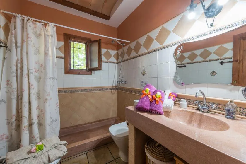 A bathroom with a tiled shower area, sink, and window.