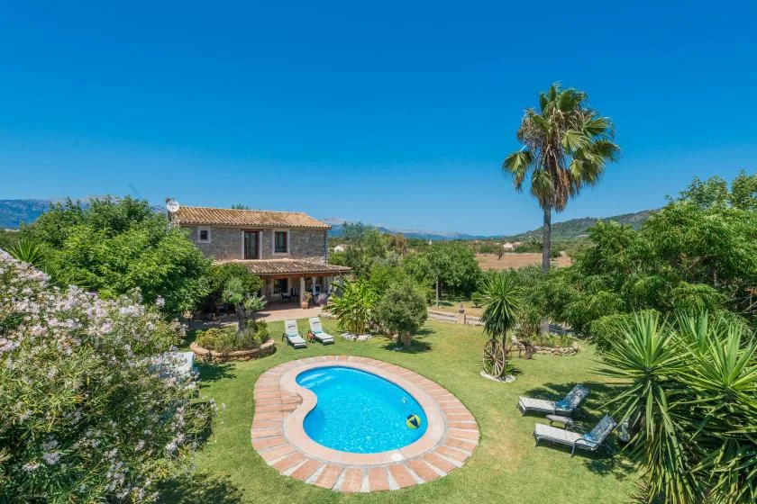 A landscaped garden surrounds a swimming pool beside a two-story house.