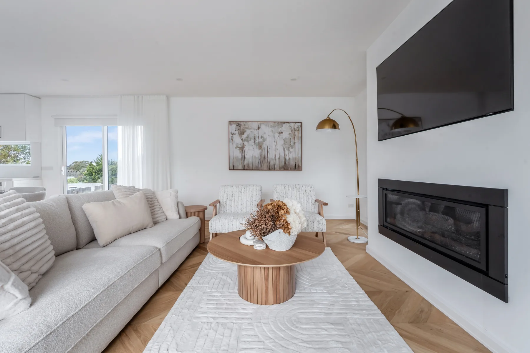 A bright living room has seating, a wall-mounted television, and a fireplace.