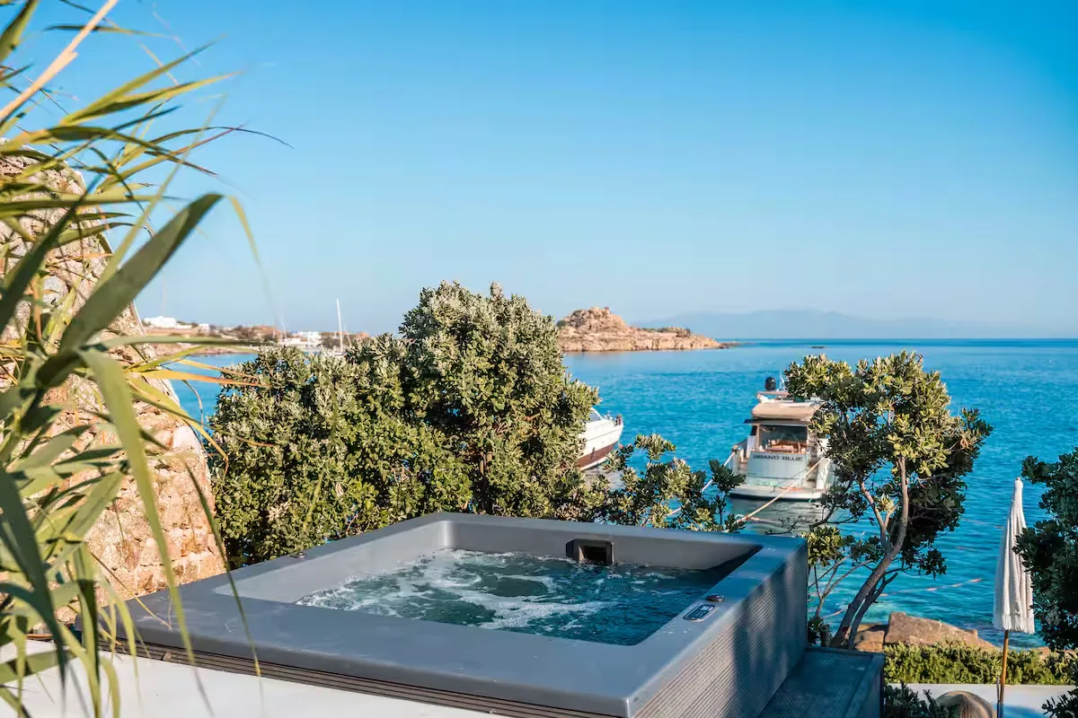A bubbling outdoor hot tub overlooks the blue sea and rocky coastline.