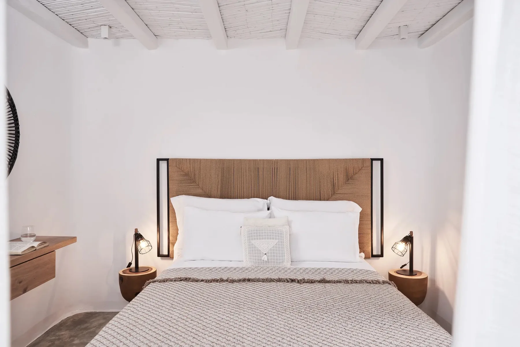 A bedroom with a bed beneath a white beamed ceiling.