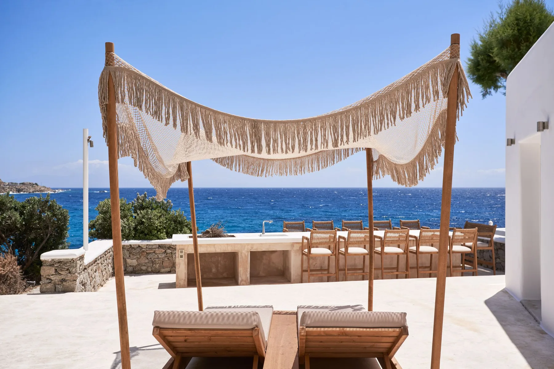An outdoor dining area with a fringed canopy overlooks the sea.