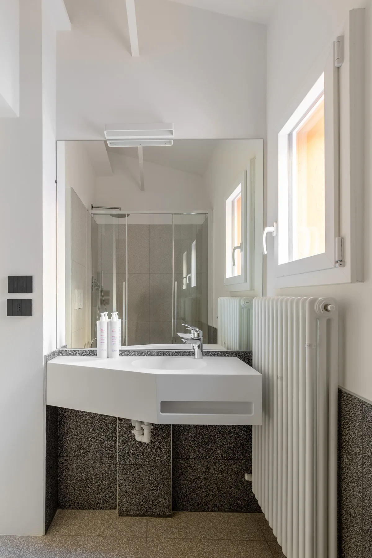Un baño luminoso con lavabo suspendido, espejo y radiador.