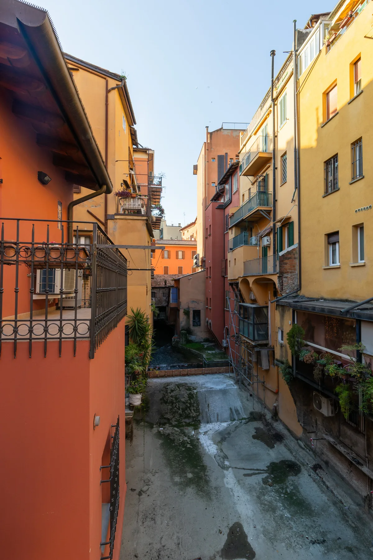 Un patio estrecho pavimentado se extiende entre edificios de apartamentos coloridos con balcones.