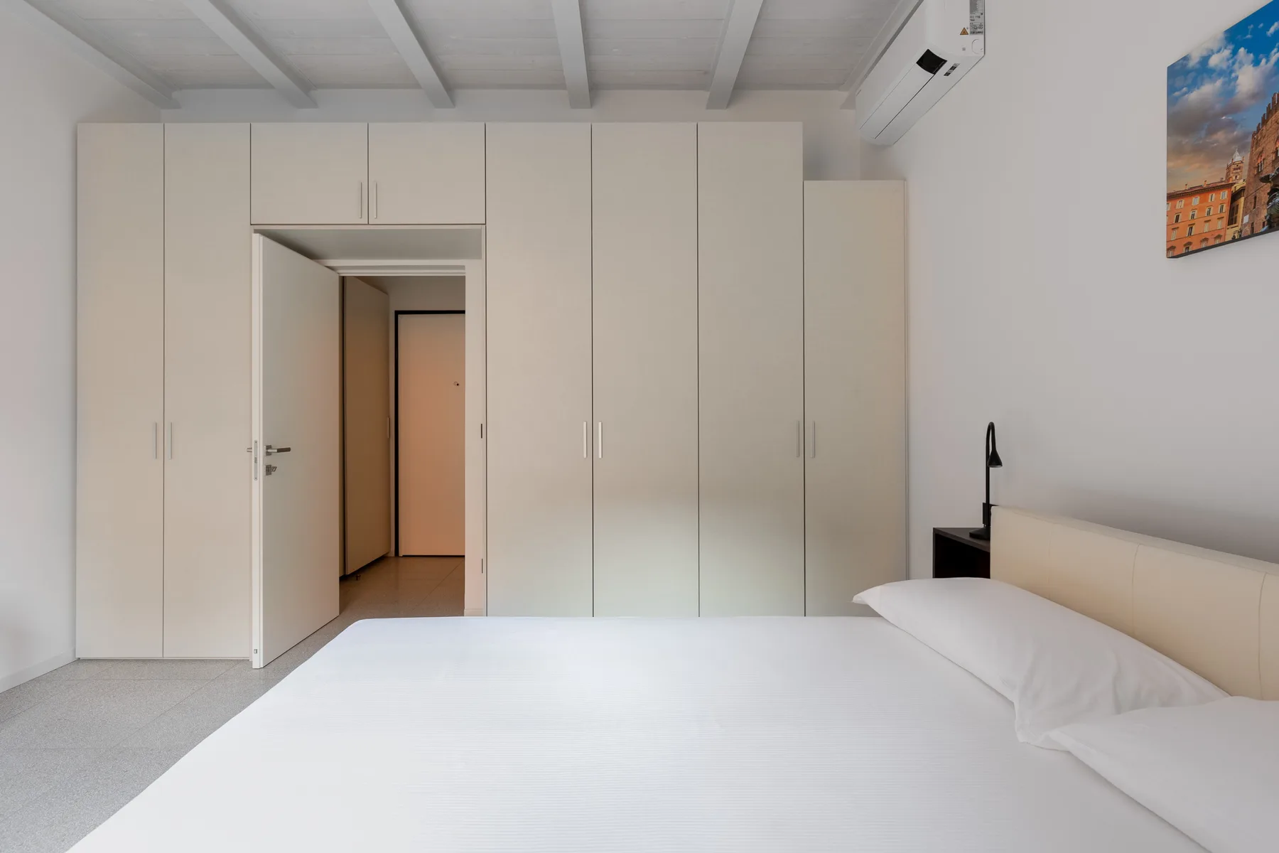 Un dormitorio con una cama blanca, armarios empotrados y una puerta abierta.