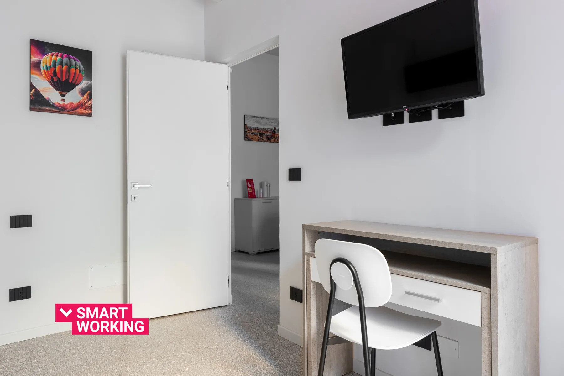 Una habitación luminosa con un escritorio, una silla y un televisor en la pared.