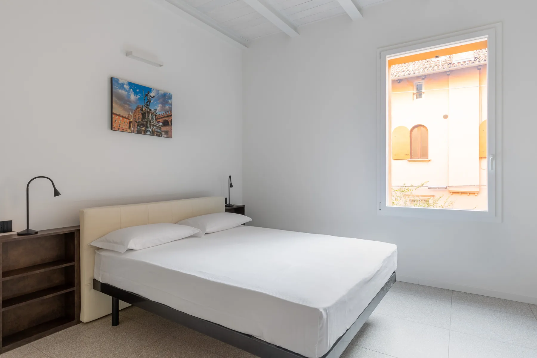 Un dormitorio luminoso con una cama tendida y una ventana que da a un patio.
