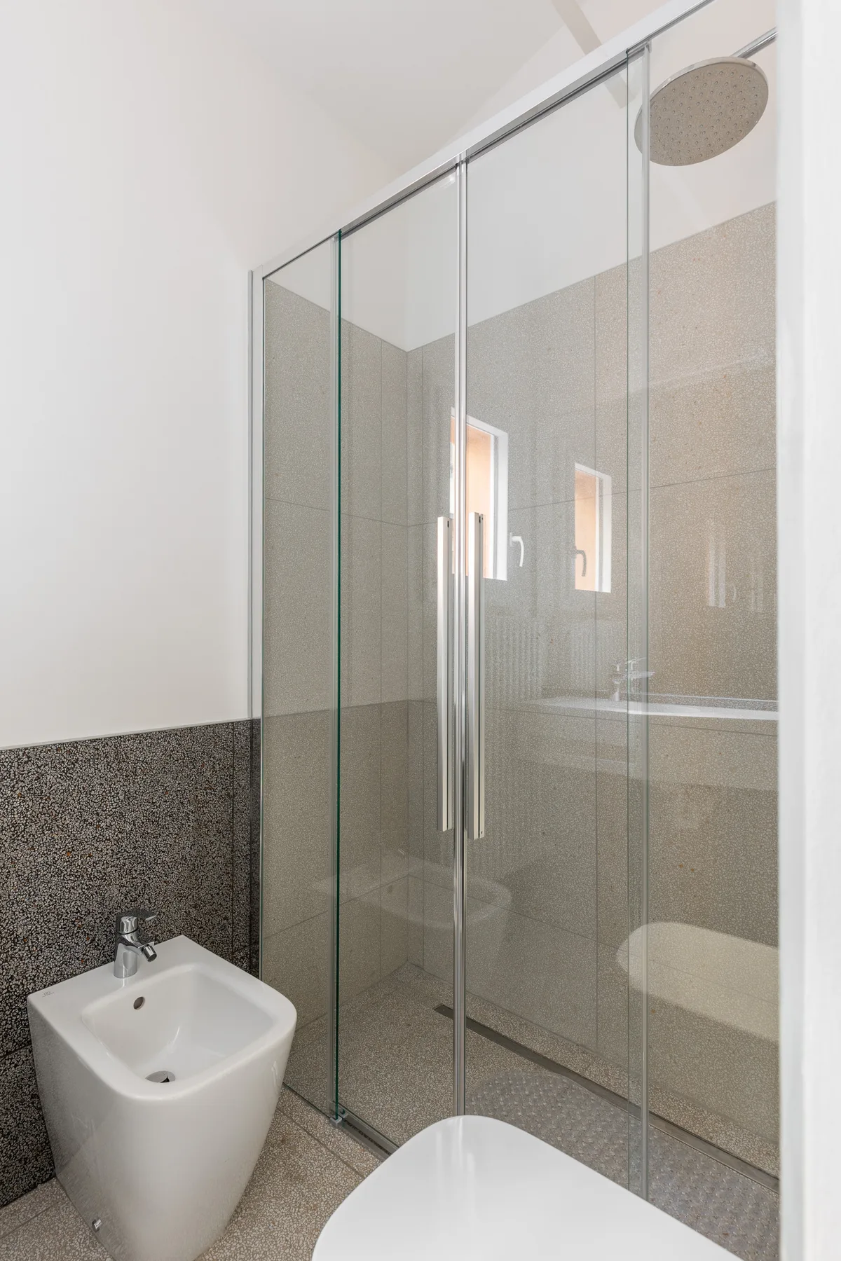 Un baño luminoso con ducha de vidrio y sanitarios de cerámica blanca.