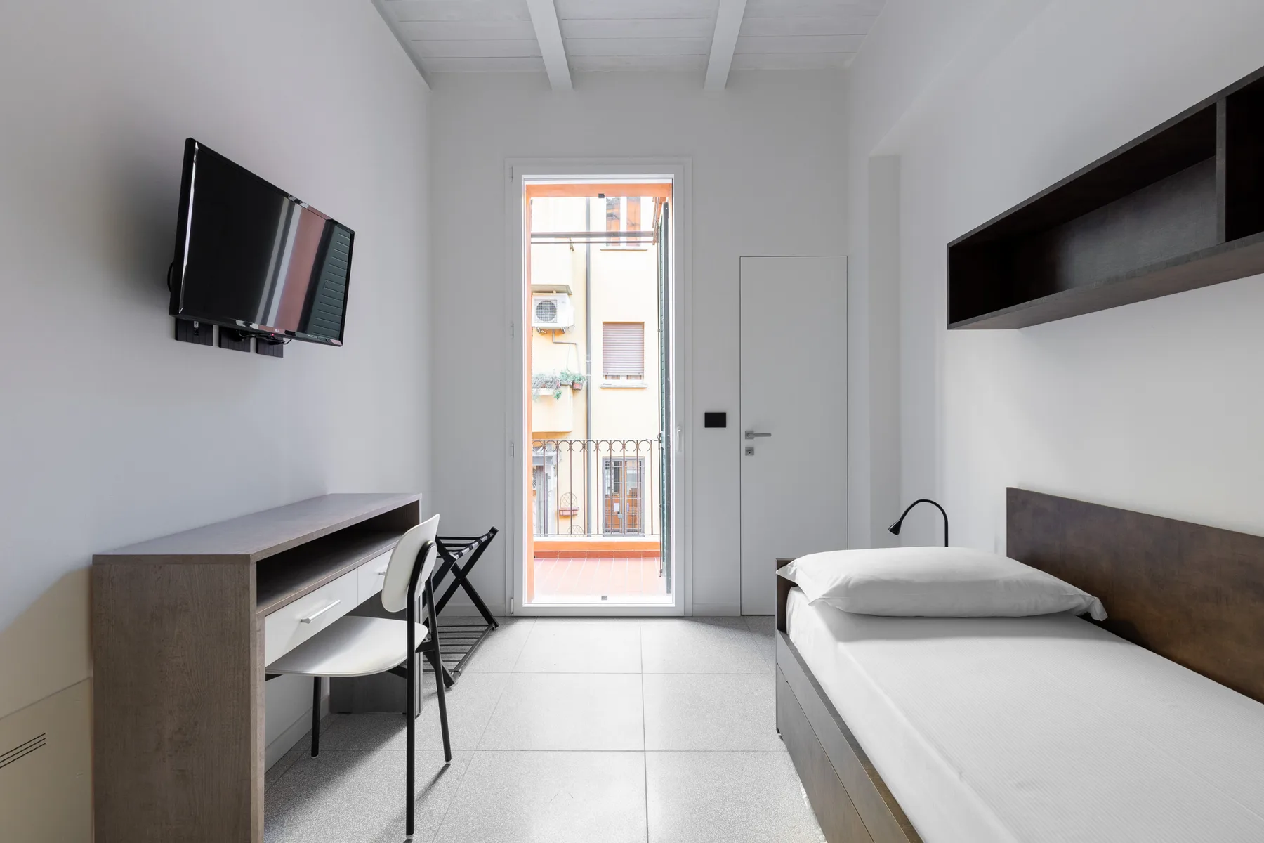 Un dormitorio luminoso con una cama individual, escritorio y televisor.