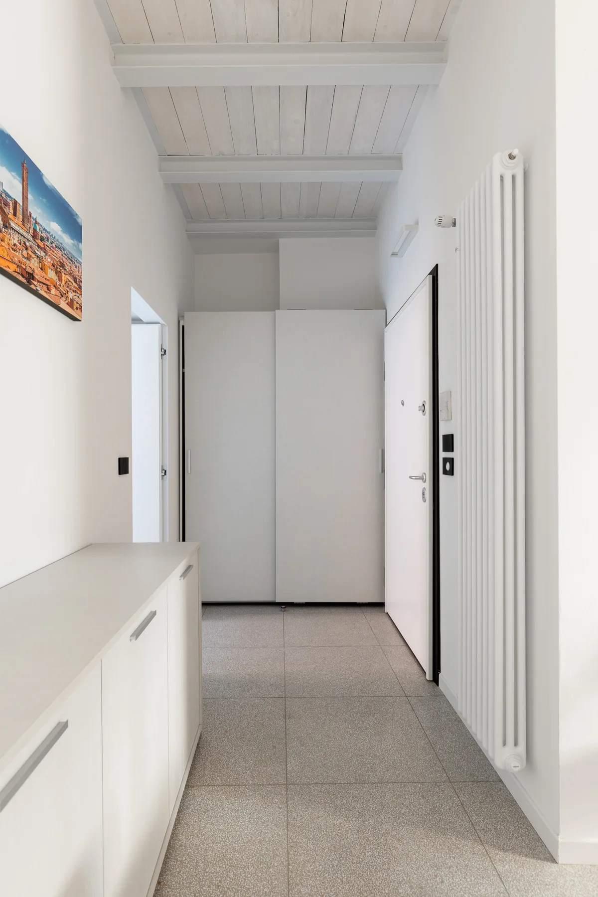 Un pasillo luminoso con armarios blancos y un radiador alto en la pared.