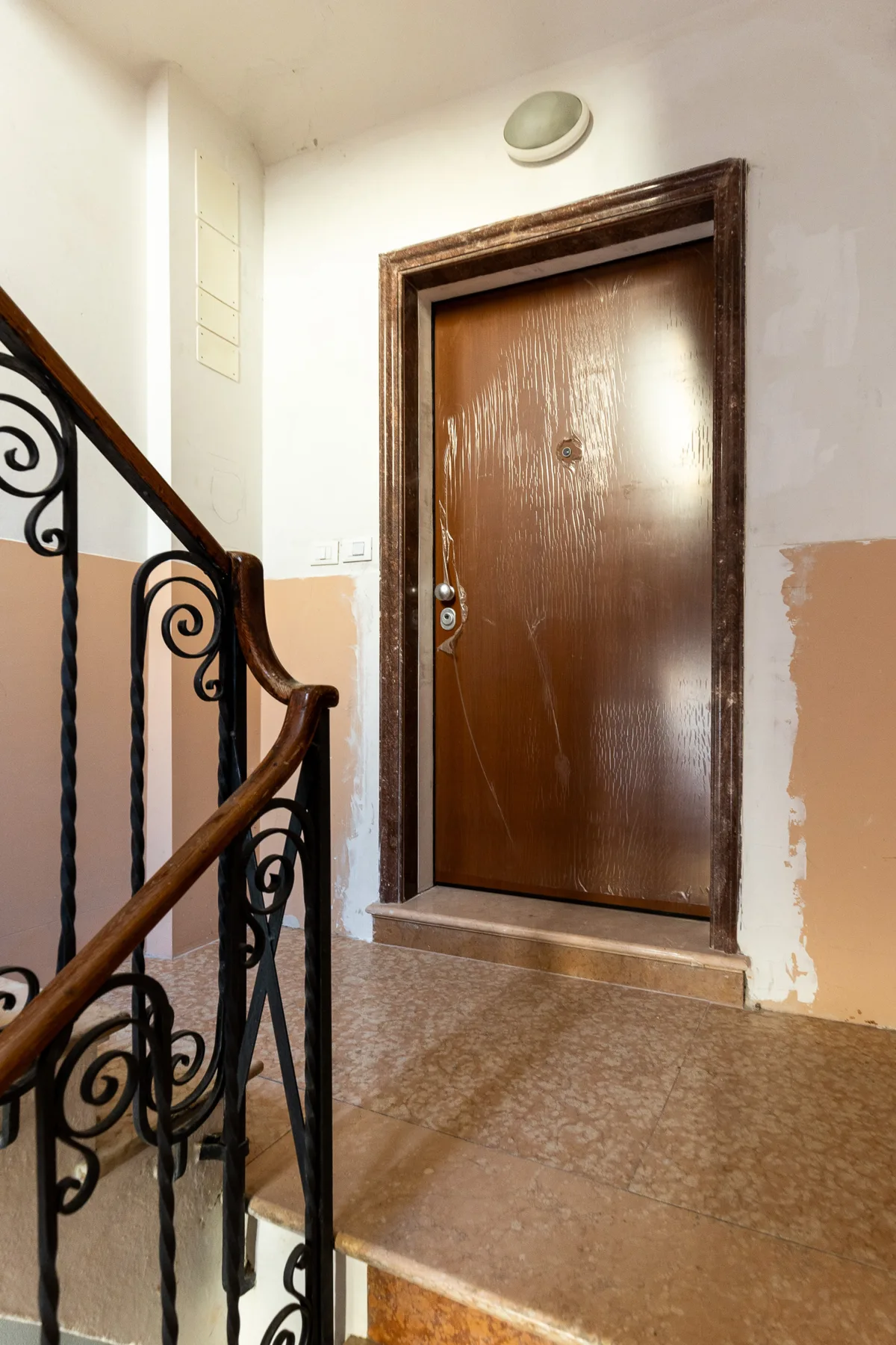 Un descansillo interior con una puerta marrón y una barandilla decorativa.