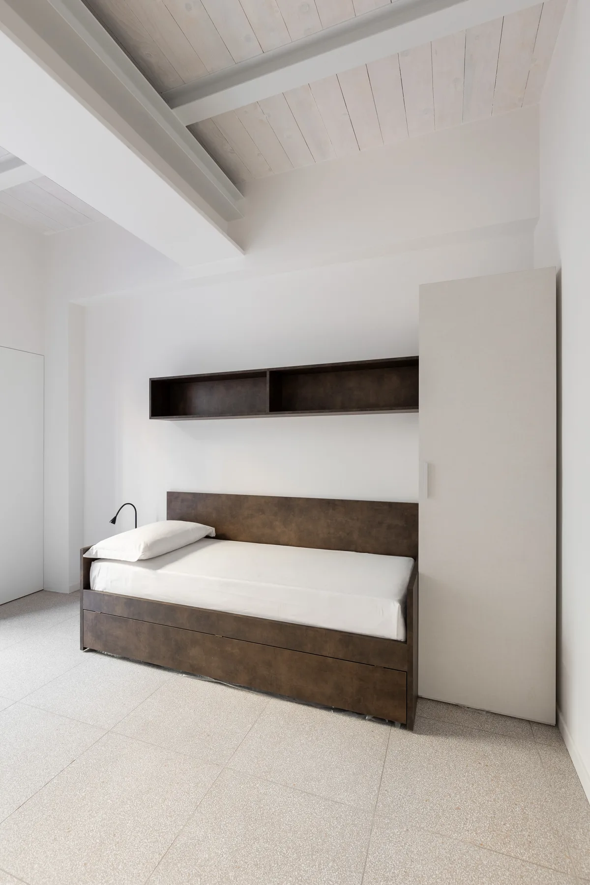 Un dormitorio con una cama bajo una repisa estrecha y vigas expuestas en el techo.