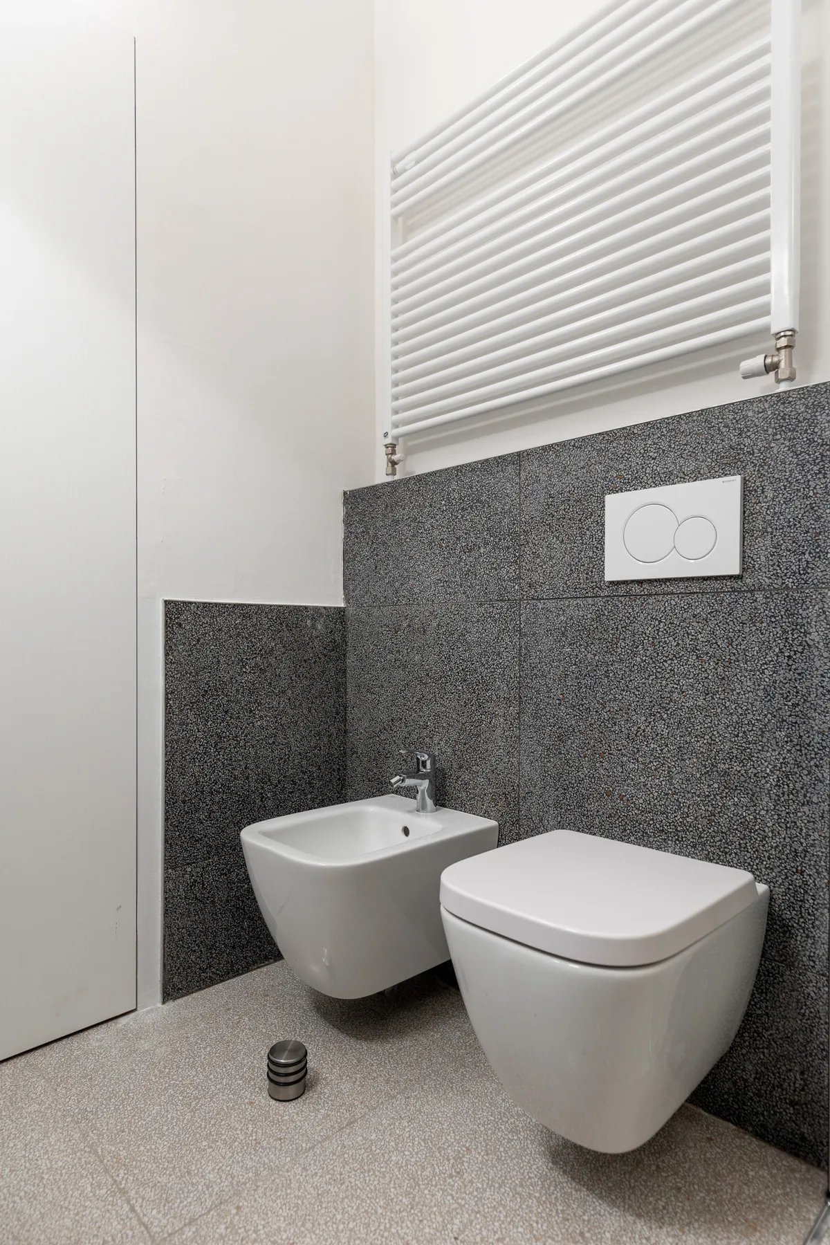 Un baño moderno con un inodoro y un bidé suspendidos bajo una persiana.