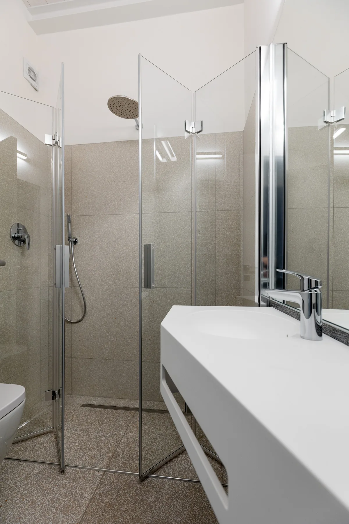 Un baño moderno con una ducha de vidrio y un lavabo blanco.