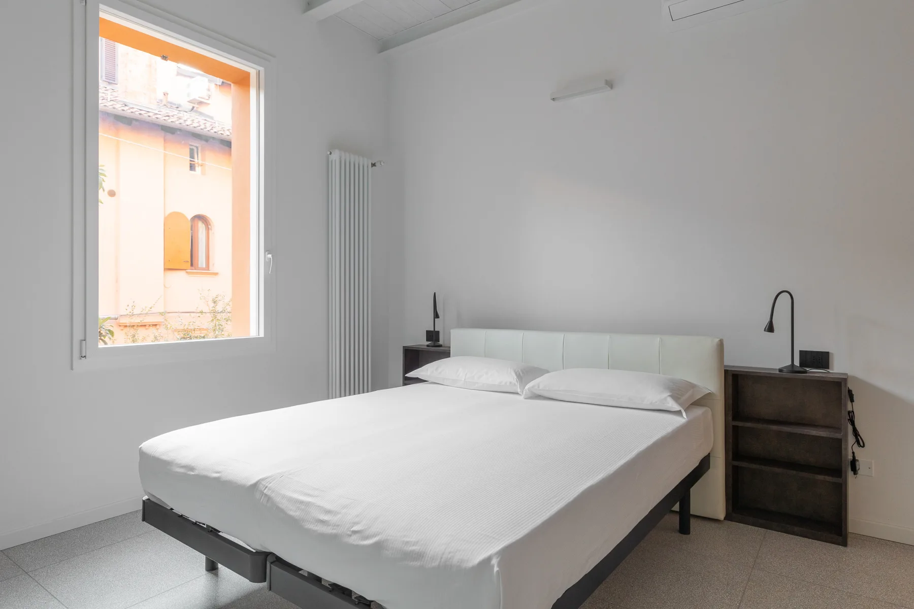 Un dormitorio luminoso con una cama junto a una ventana y una mesita de noche.