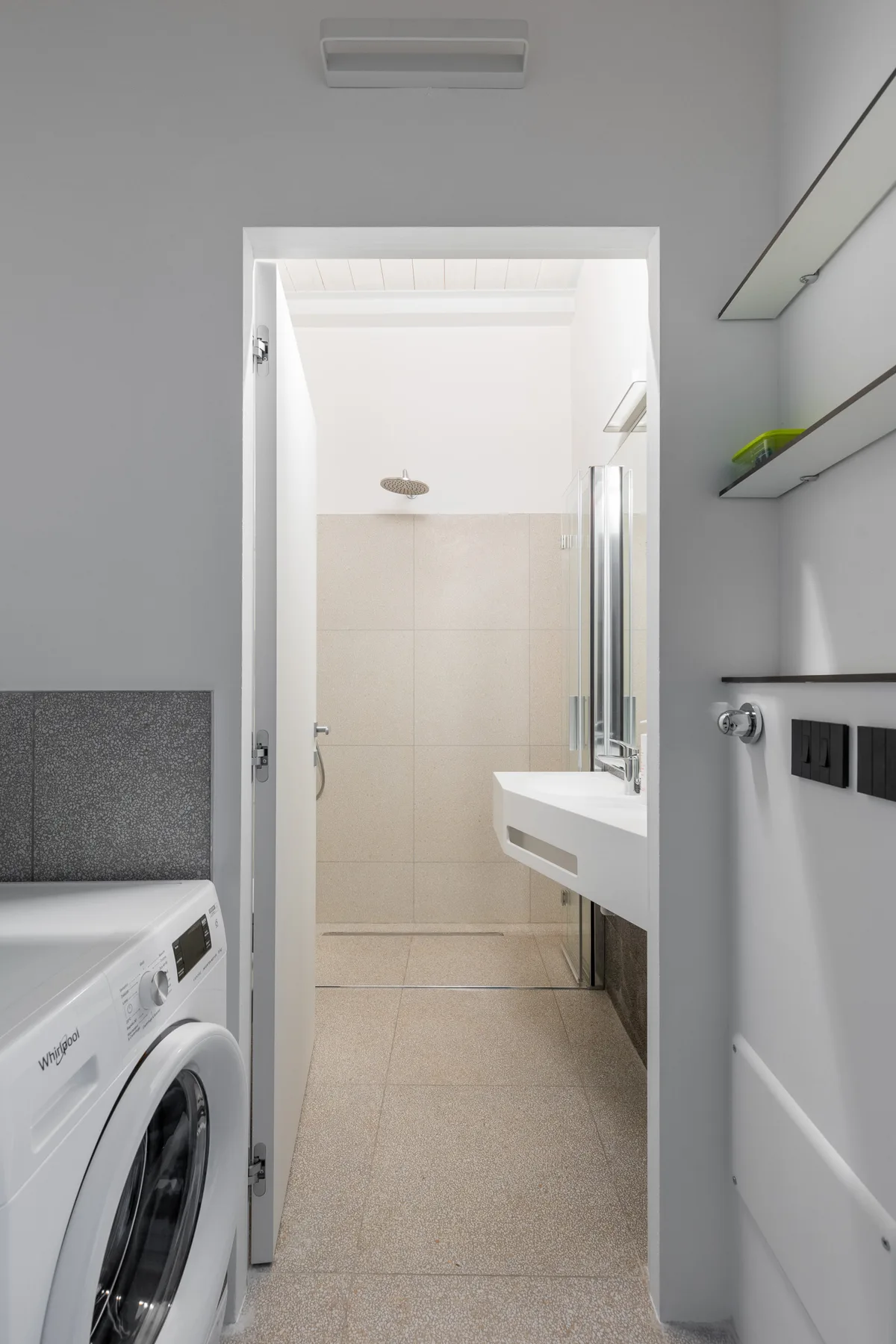 Una zona de lavandería da a un baño alicatado con ducha y lavabo.
