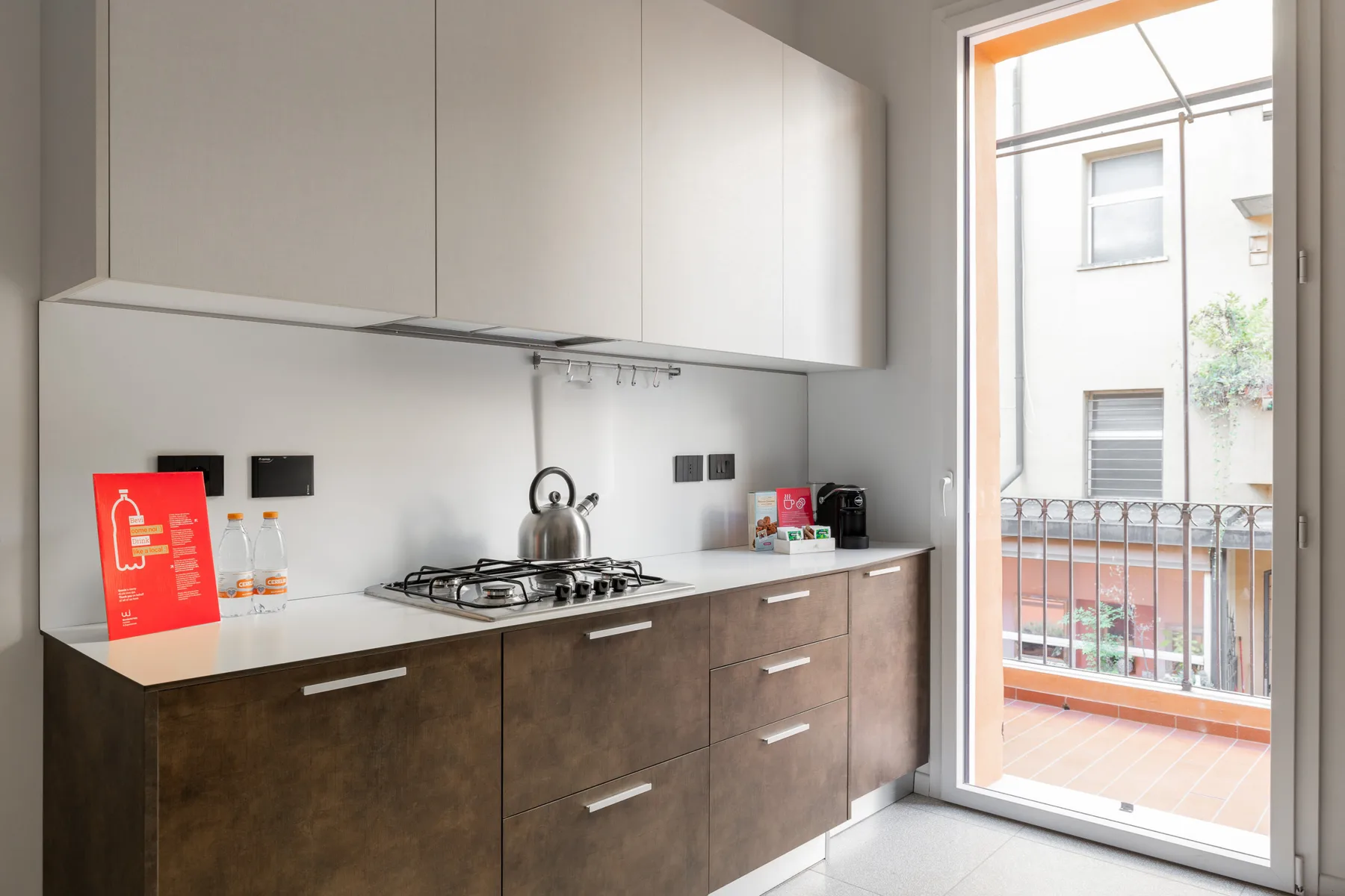 Una cocina moderna con gabinetes, una placa de cocina y una tetera junto a una puerta de vidrio.