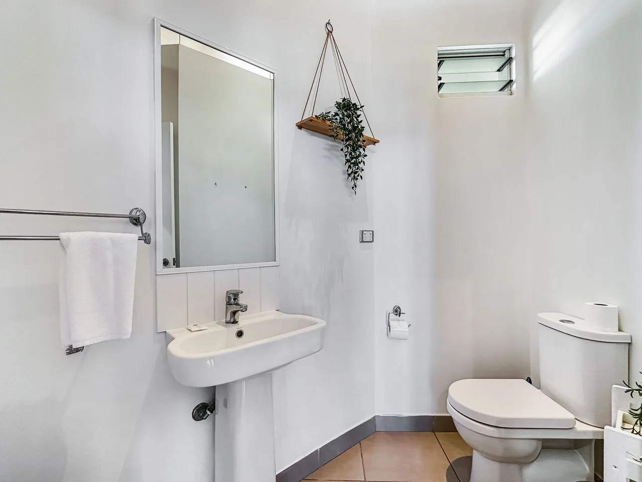 Un baño luminoso con lavabo de pared e inodoro.