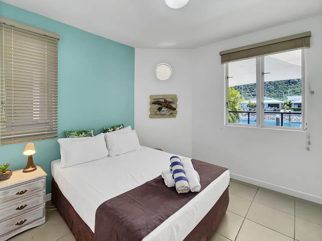 Dormitorio con una cama tendida y una ventana con vista a una piscina.