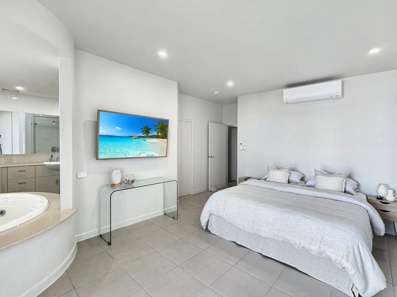 Un dormitorio luminoso con una cama grande y un televisor montado en la pared.