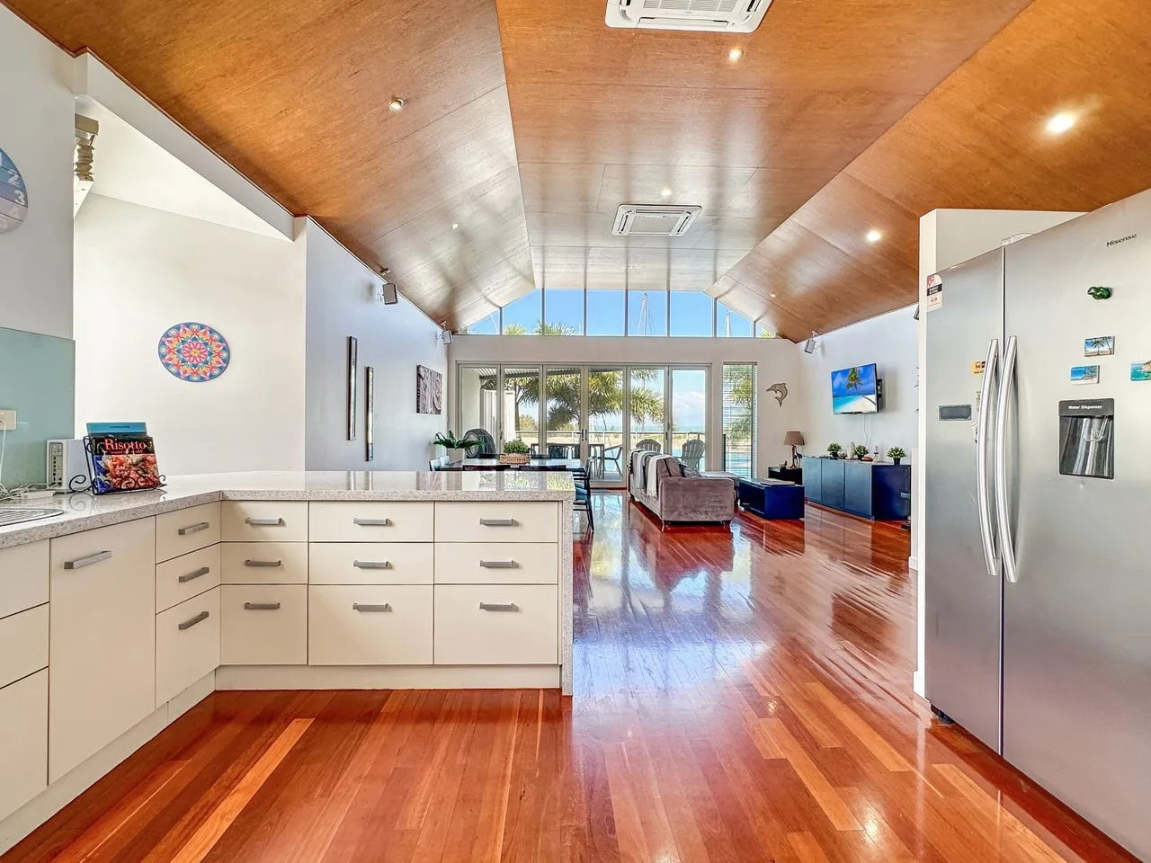 Cocina y sala de estar abiertas con piso de madera y techo alto inclinado.