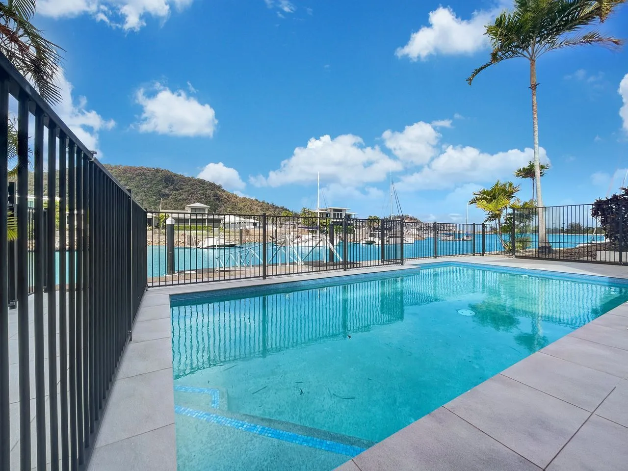 Una piscina al aire libre está junto a un área cercada bajo un cielo azul.