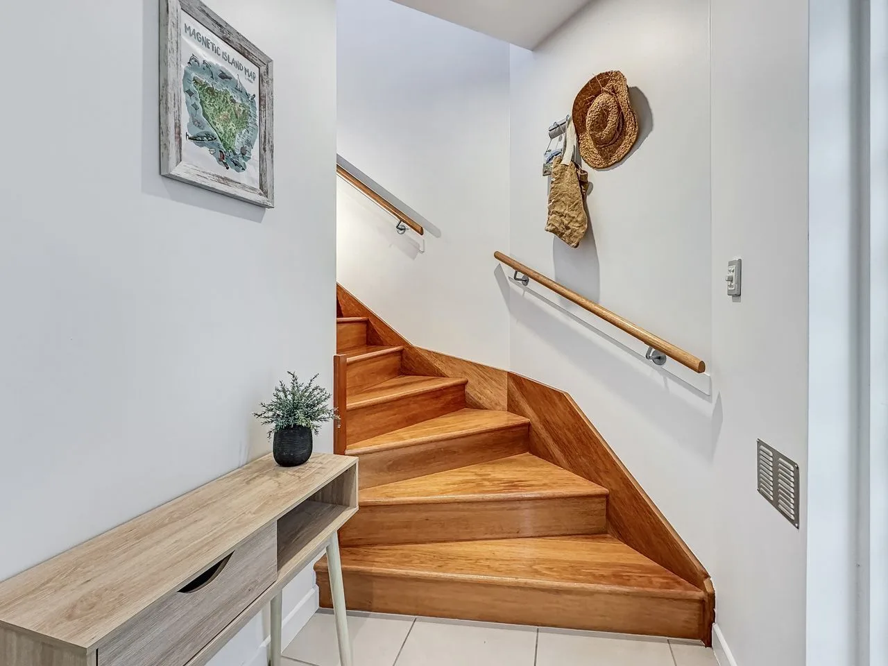 Una escalera de madera con pasamanos sube junto a una consola estrecha.