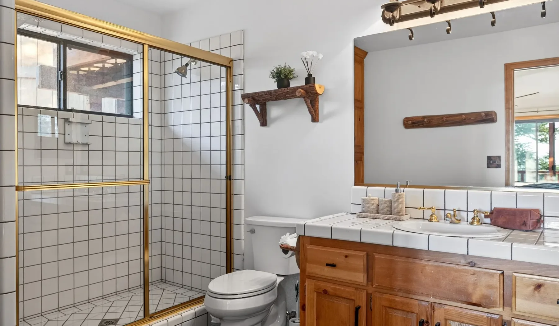 A tiled bathroom with a glass shower, toilet, and wooden vanity beneath a large mirror.