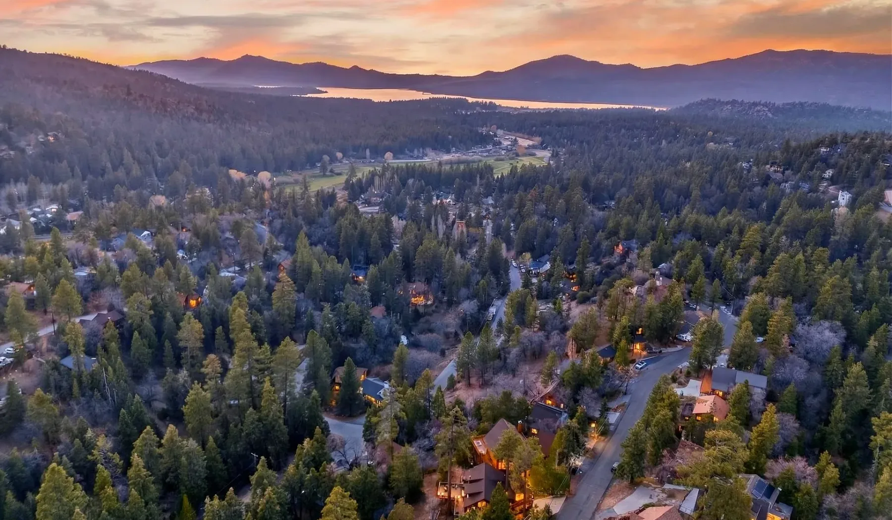 An aerial view of a wooded neighborhood beneath distant mountains at sunset.
