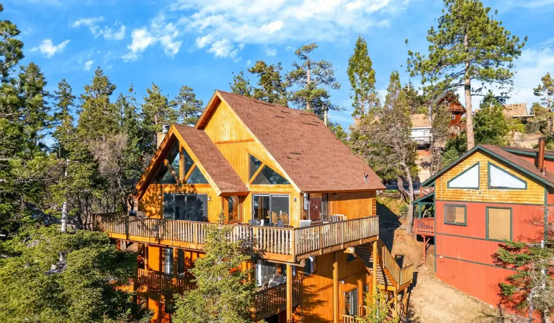 A wooden cabin with a broad deck sits among tall trees.