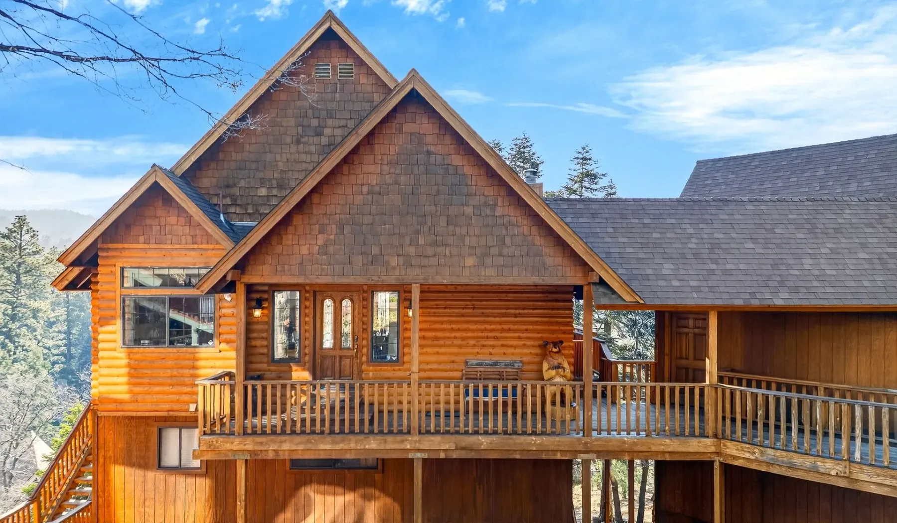 A large wooden house with steep gables and a long balcony beneath a blue sky.