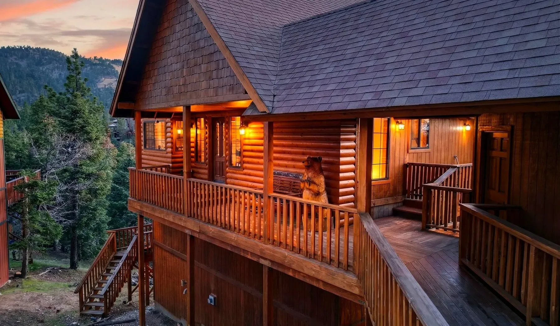 A wooden cabin with a covered porch overlooks a forested hillside at dusk.