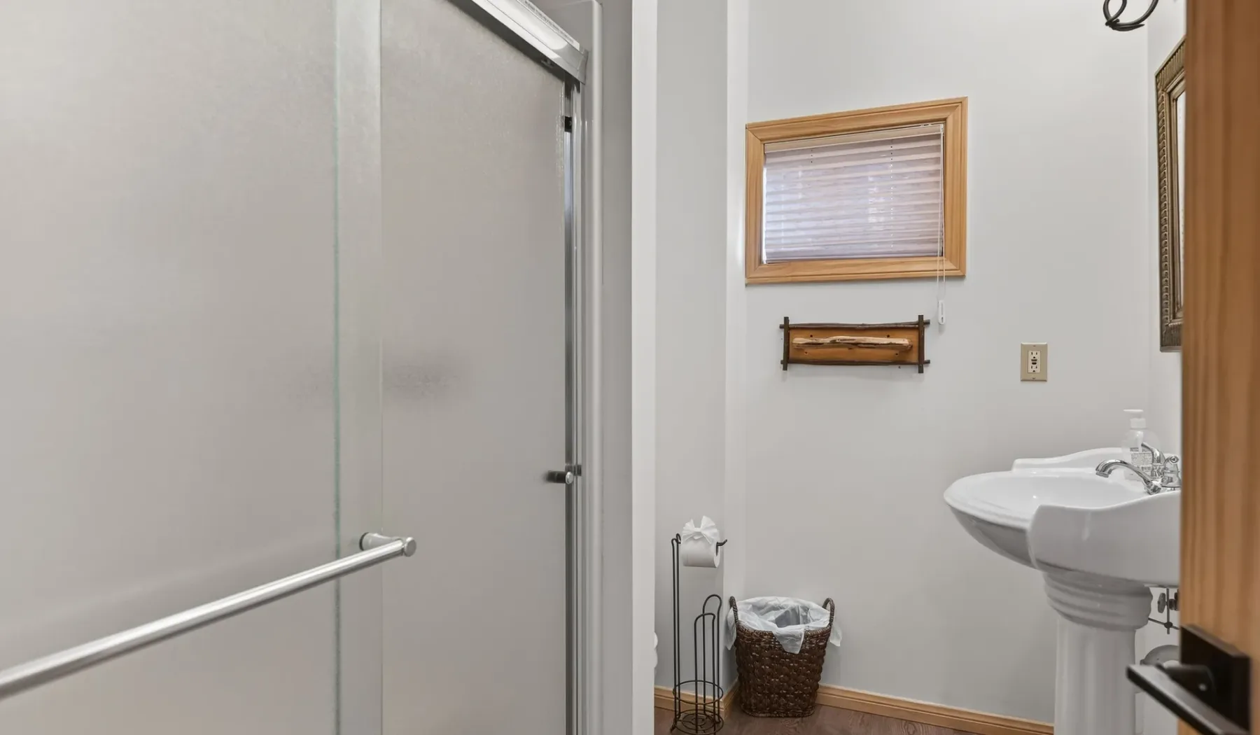 A bathroom with a shower, sink, and small window.