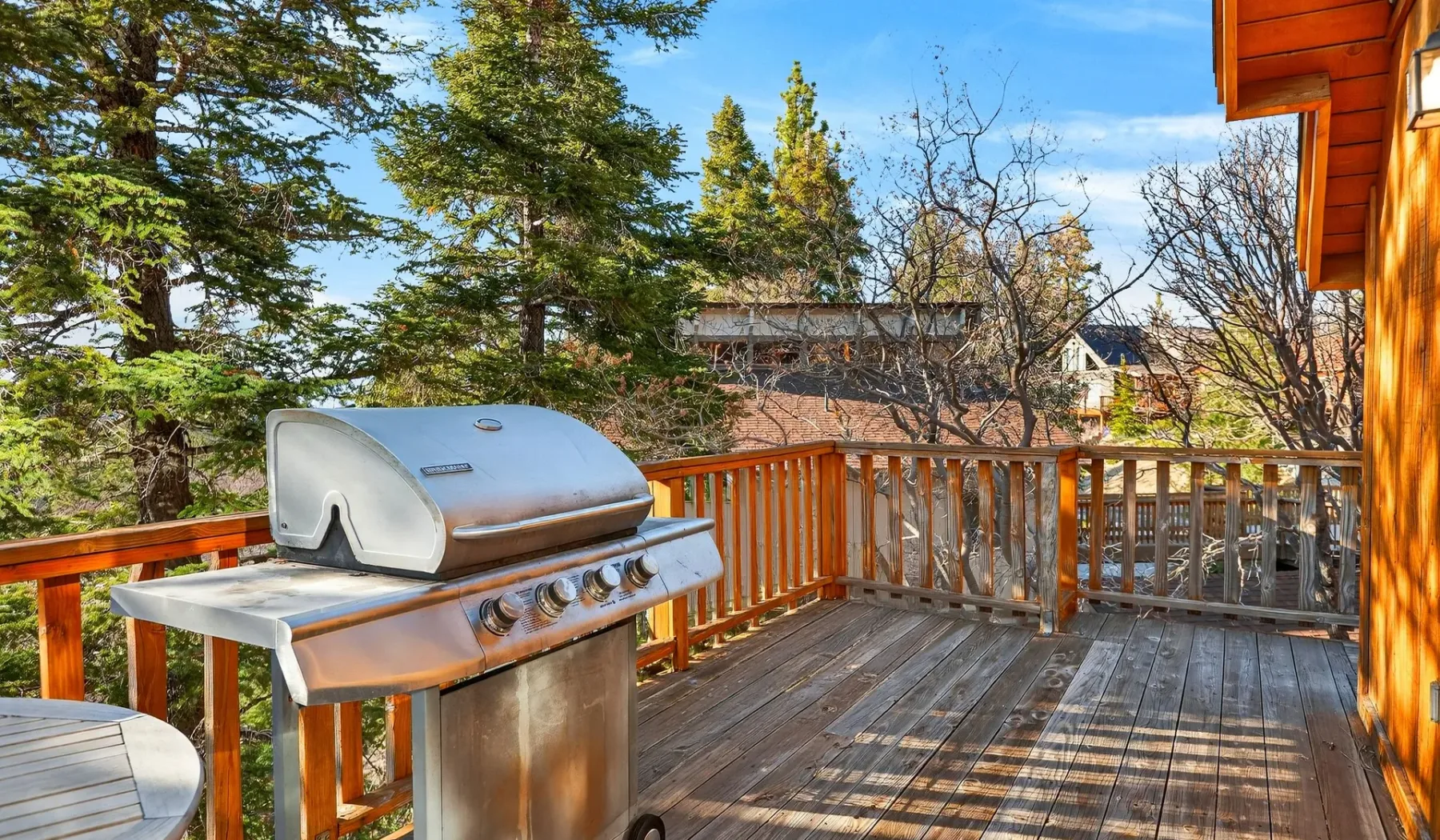 A wooden deck with a covered barbecue grill and trees beyond the railing.