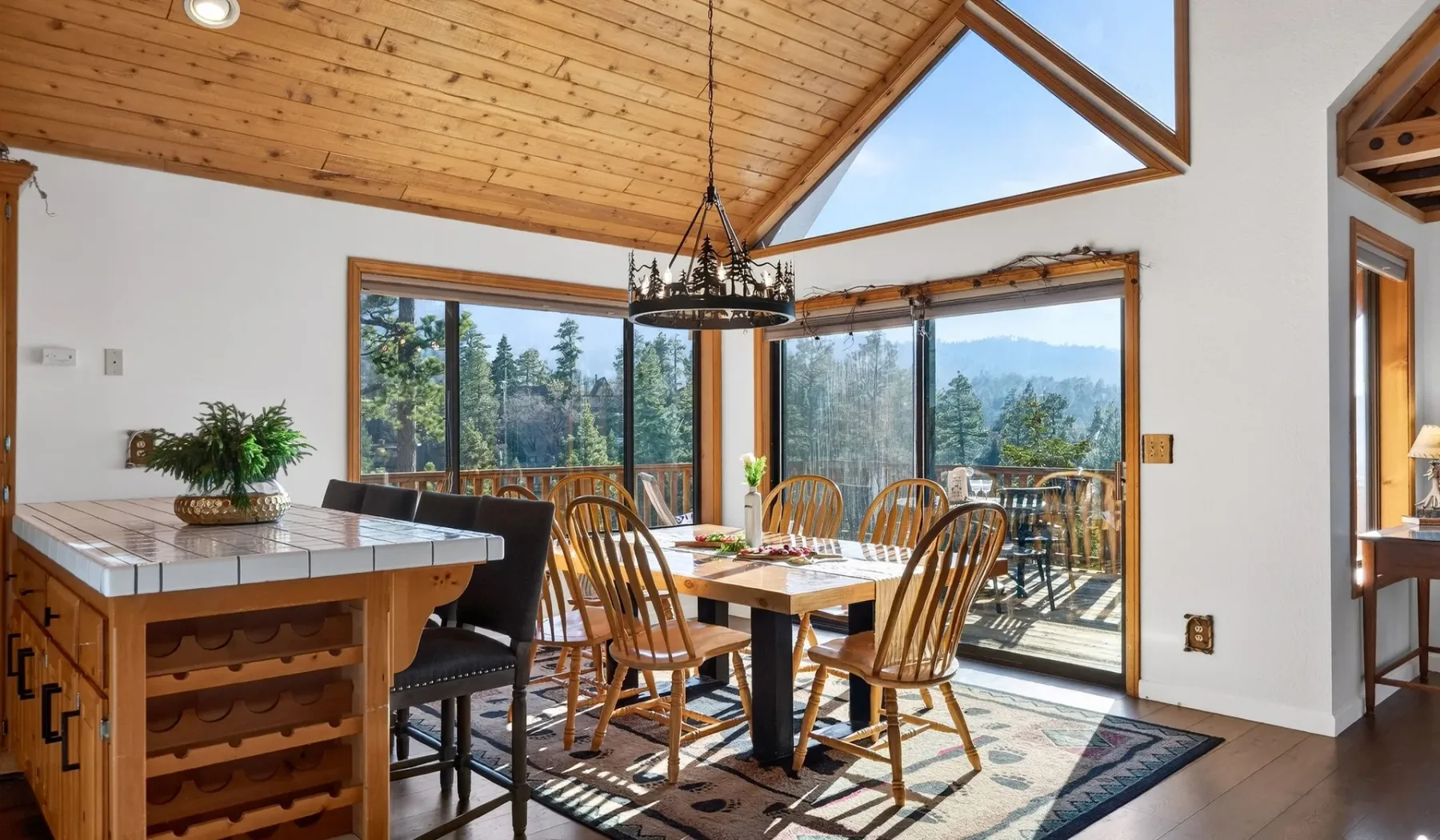 A dining area with a wooden table and large windows overlooking a wooded view.