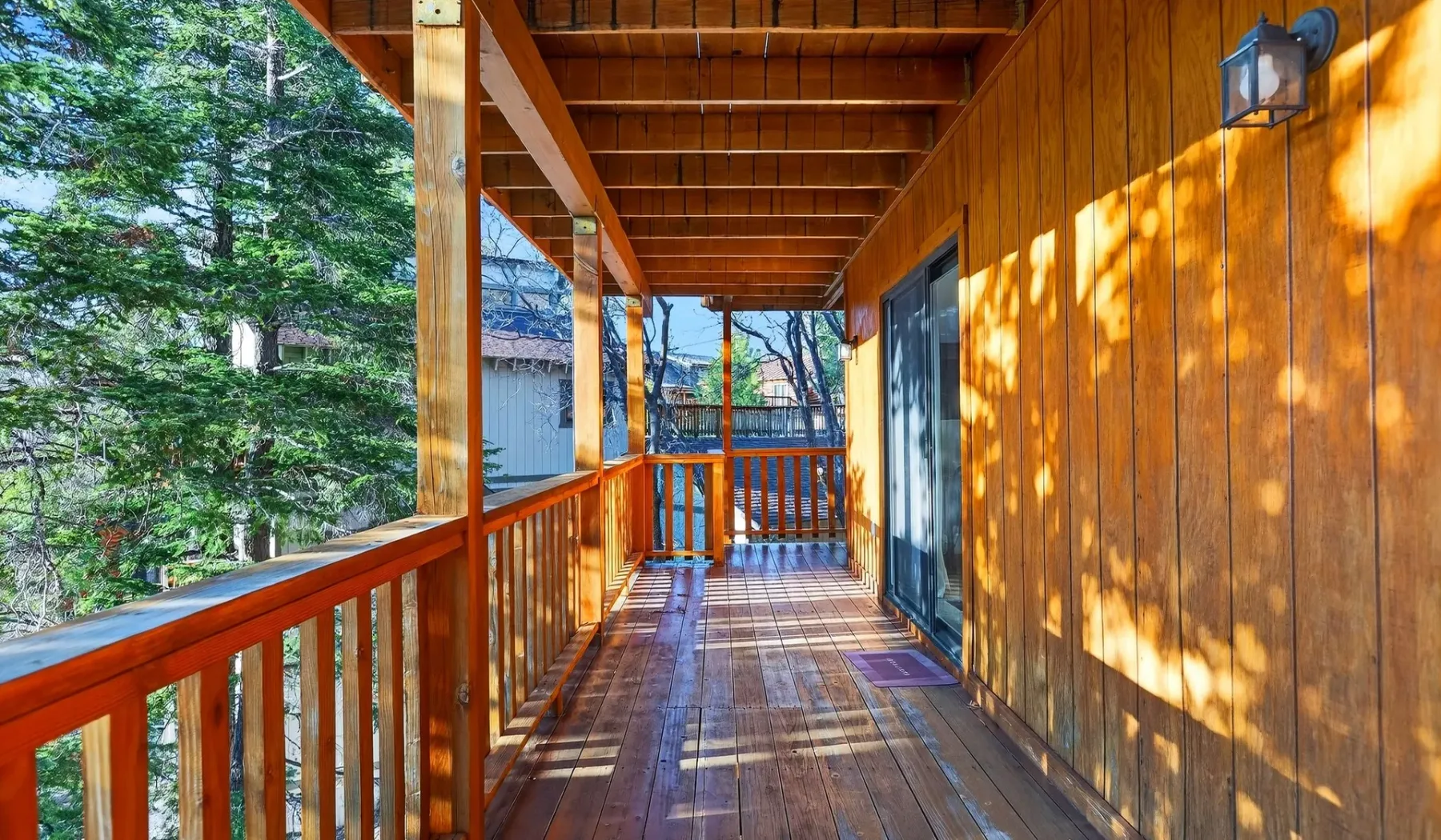 A covered wooden porch runs alongside a building, with trees visible beyond the railing.